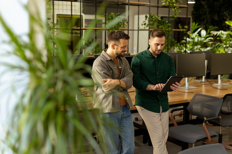 Two professionals are engaged in a focused conversation while holding digital tablet in a contemporary office space, featuring rustic exposed brickwork and warm natural light